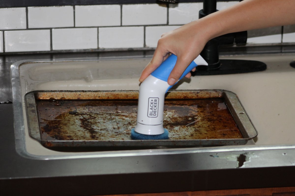 Person using Black and Decker power scrubber to clean a sheet pan