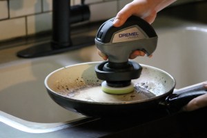 Person using Dremel power scrubber to scour tough stains from a pan