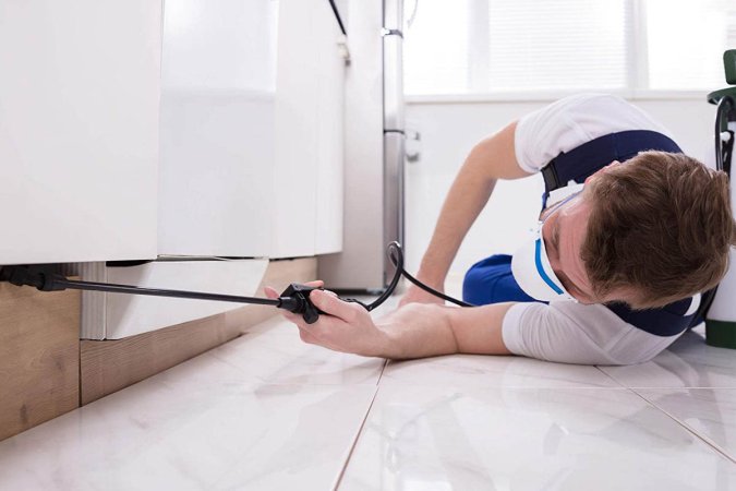 Man spraying chemicals under a kitchen counter