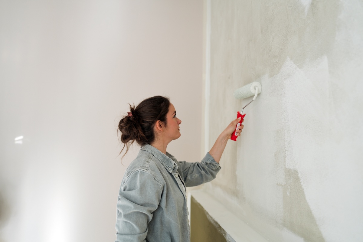 A woman uses primer on an off-white wall with a sponge roller brush.