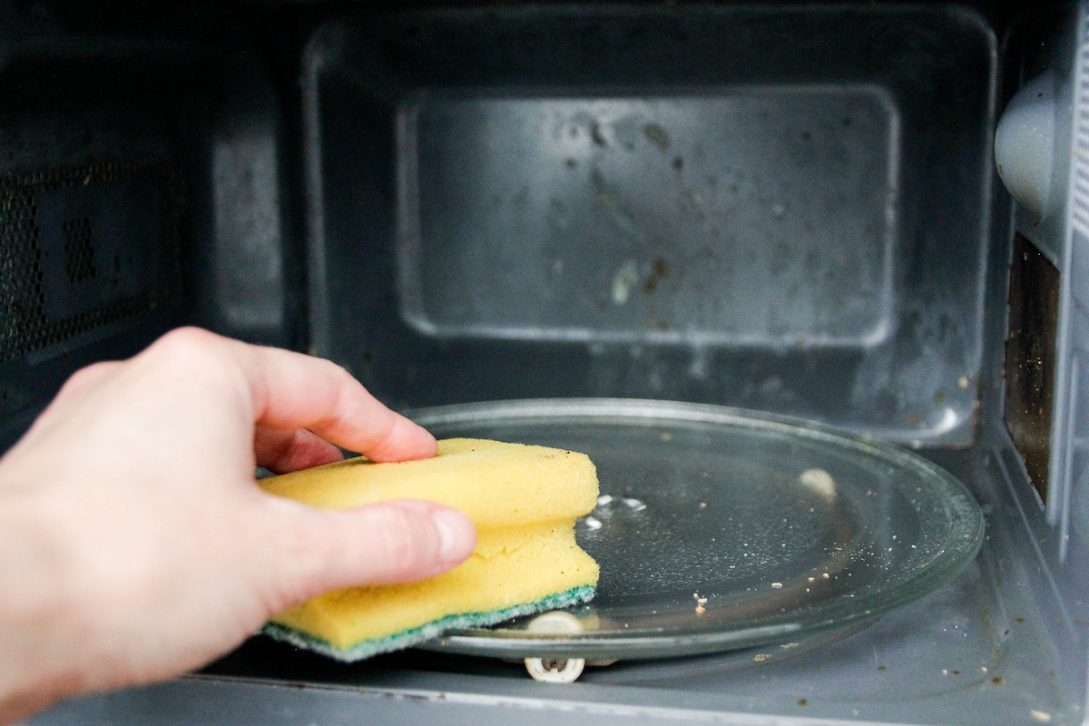 Somebody cleaning the interior of a microwave with a sponge.