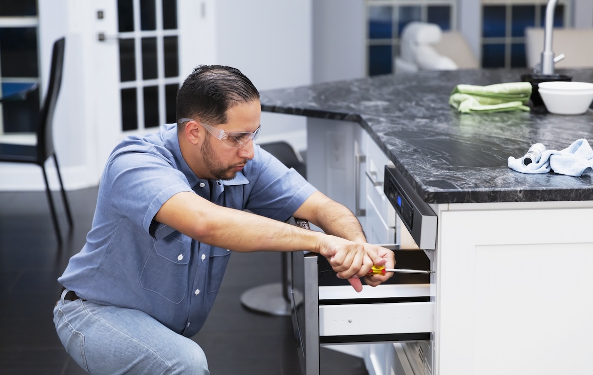 A repairman in safety glasses repairs a pull-out drawer style microwave.