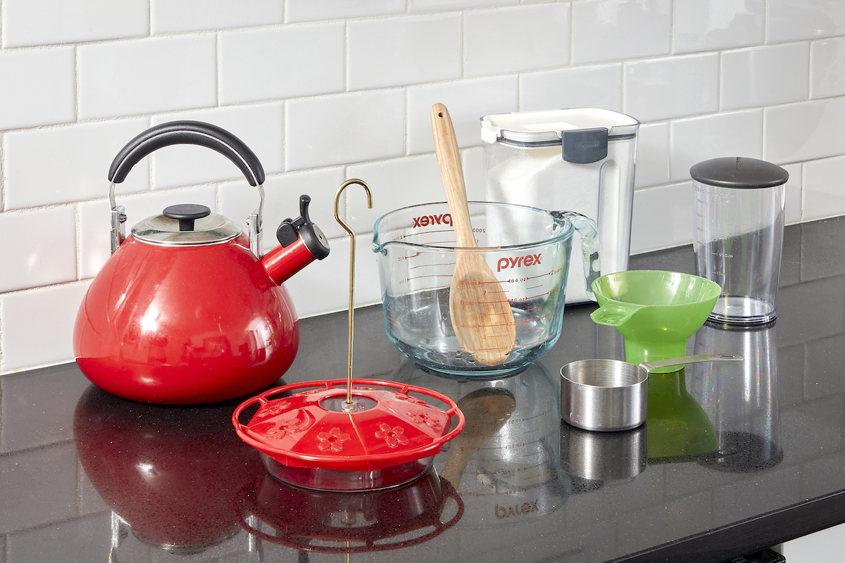 On a kitchen counter, tools and materials needed to make hummingbird food, including teakettle, measuring cup, and sugar.