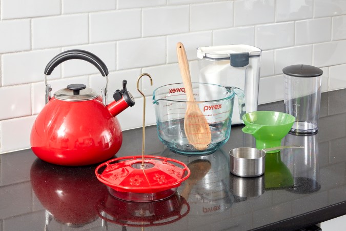 On a kitchen counter, tools and materials needed to make hummingbird food, including teakettle, measuring cup, and sugar.