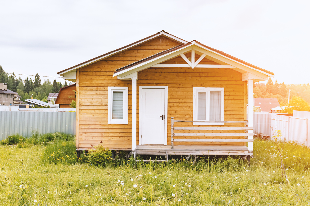 Small tiny wooden frame house with sundeck and white windows and door as a country residence in sunny summer day.