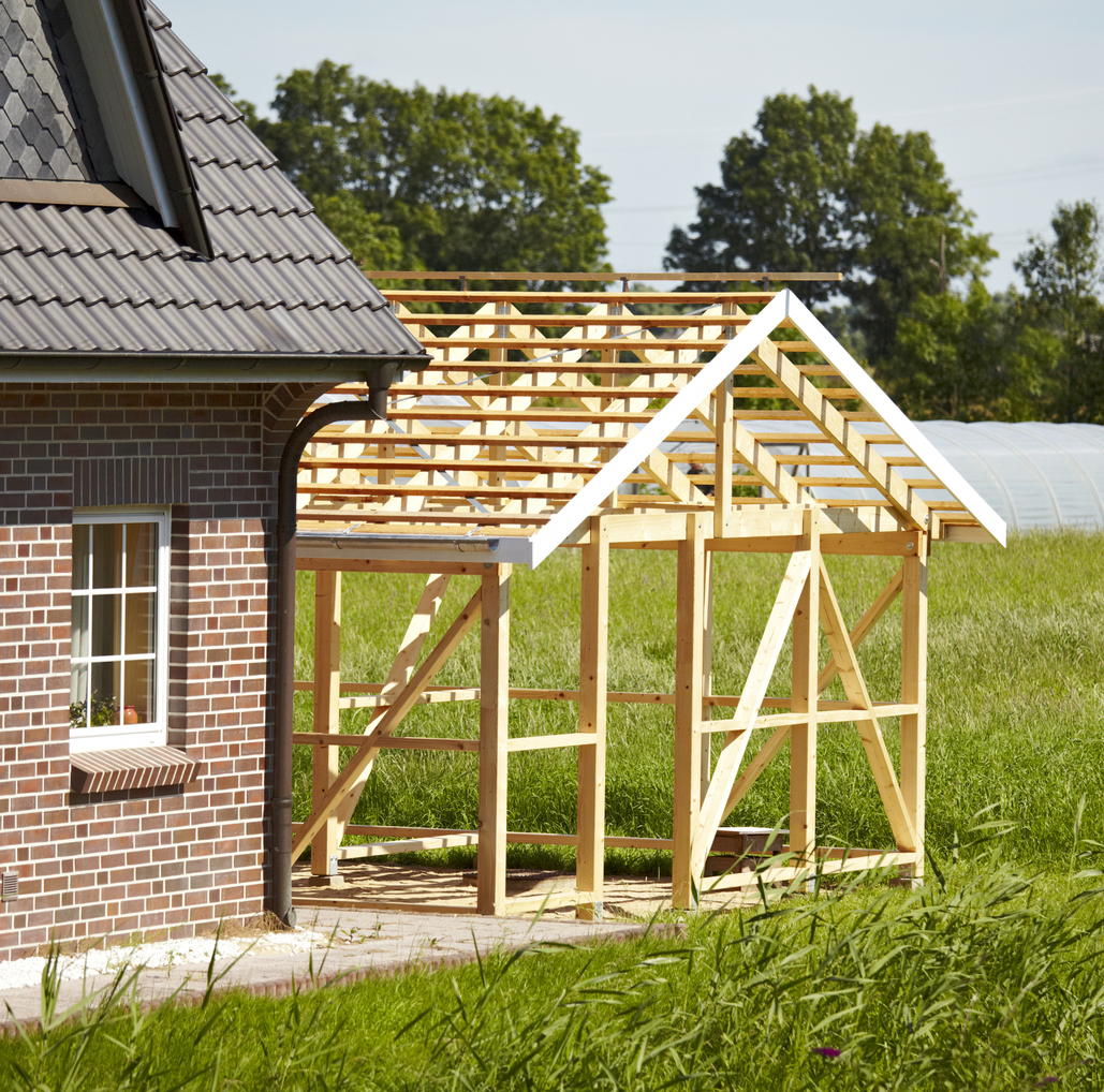 outdoor shot in sunshine. a part from a timber frame construction. outdoors in sunshine. close up of a part of a family home. green landscape in background.On the right side you can see a new wooden scaffolding. here is a growing place