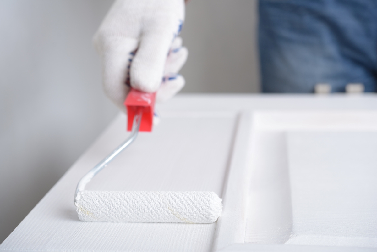 Person using roller to paint door white