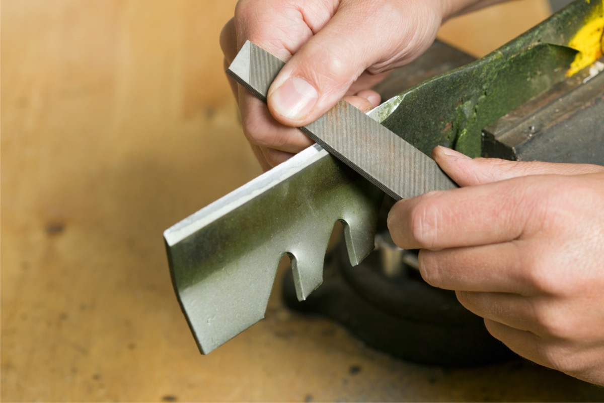 A person is sharpening a lawn mower blade with a tool.