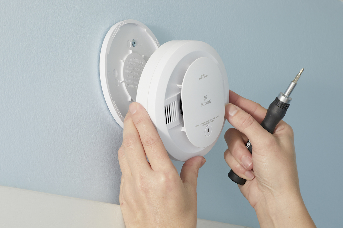 Woman removes smoke alarm from wall bracket with a screwdriver.