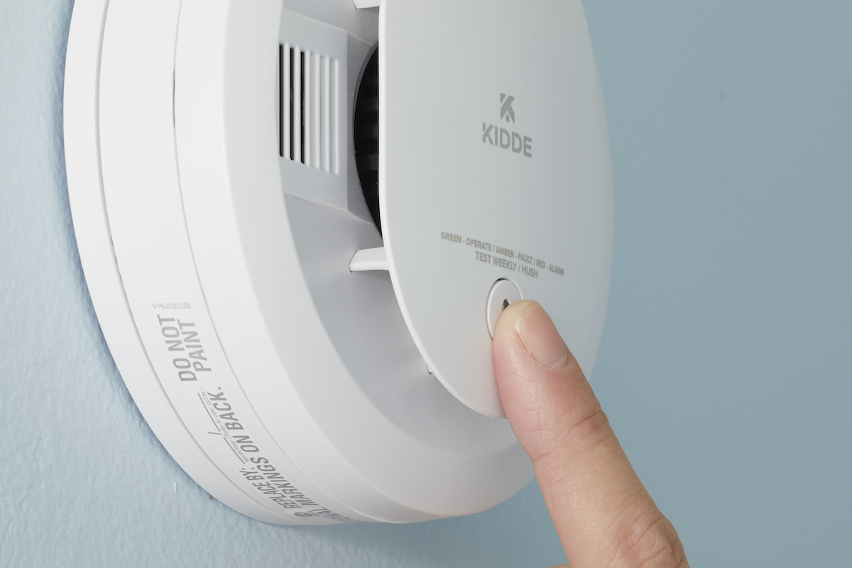 Woman presses the "test/hush" button on her smoke alarm.