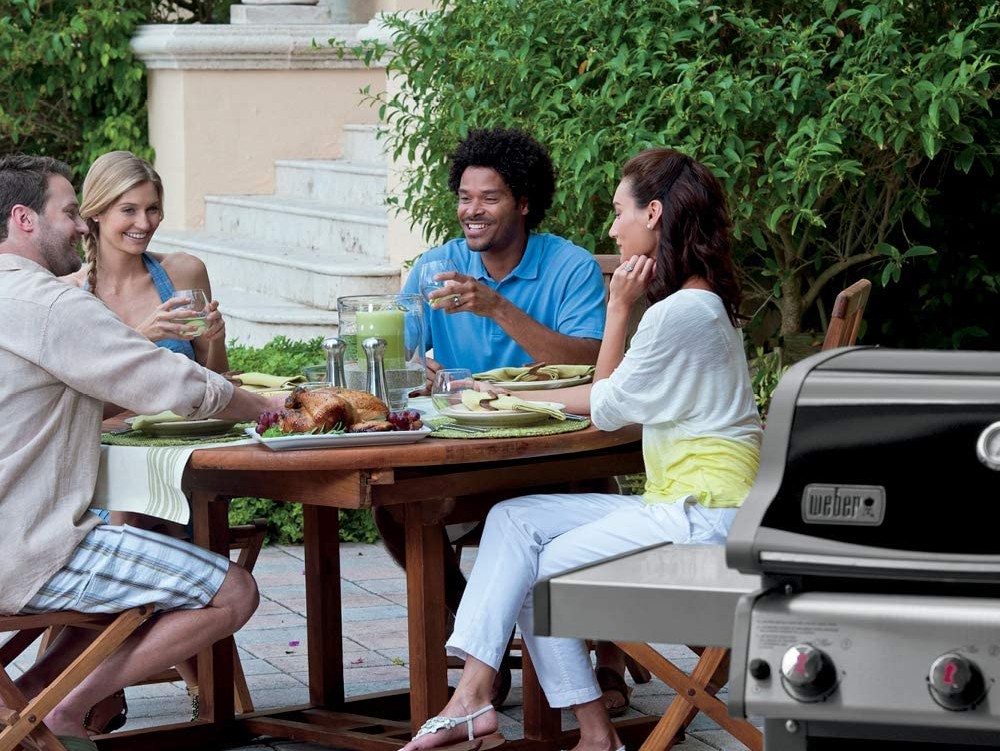 Four people eating outdoors at a round dining table next to a Weber grill
