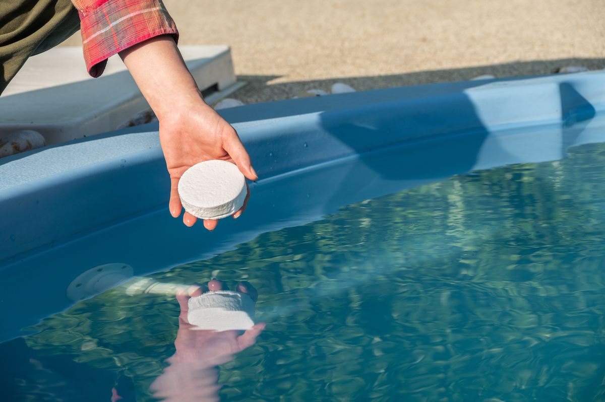 A person is placing a chlorine tablet into a swimming pool.