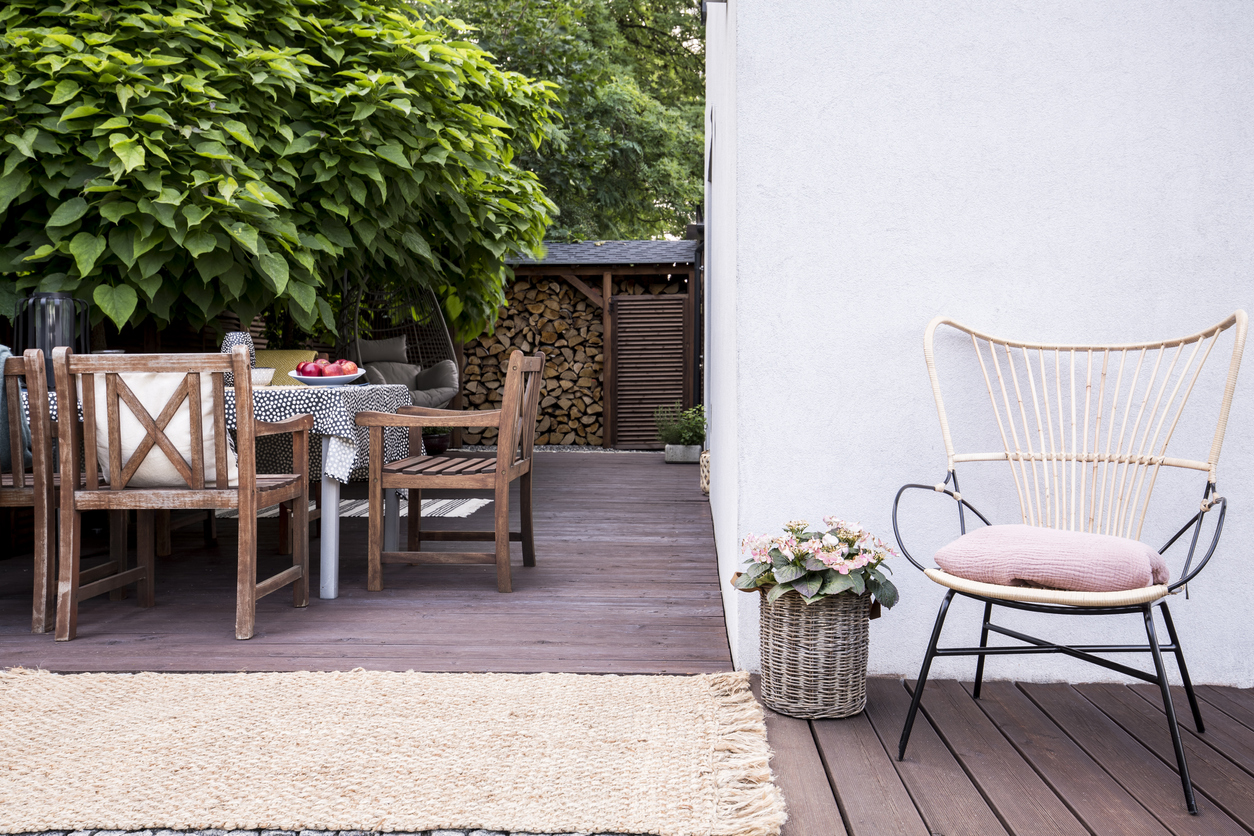 Pink flowers next to armchair on wooden terrace with chairs at table next to tree