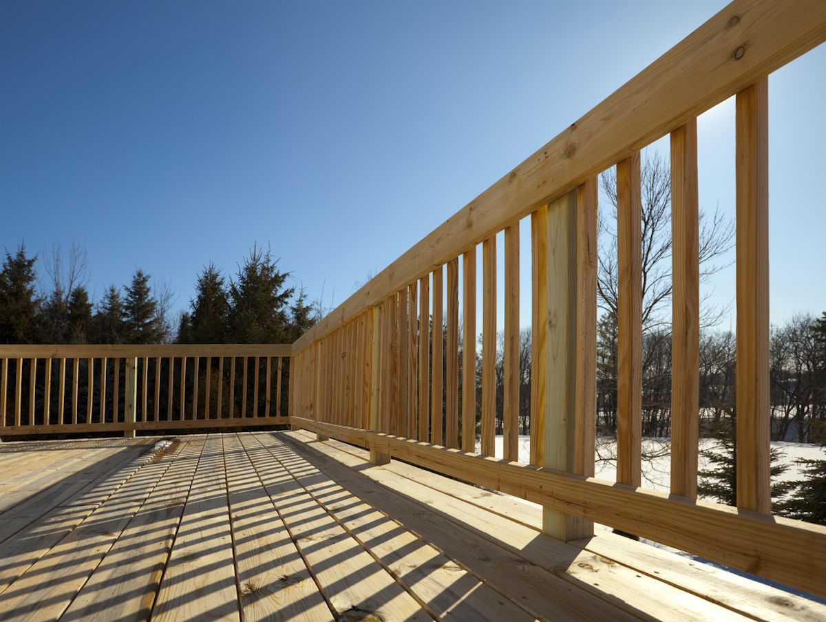 Unpainted wood deck railing with wood deck treads against a dark blue sky.