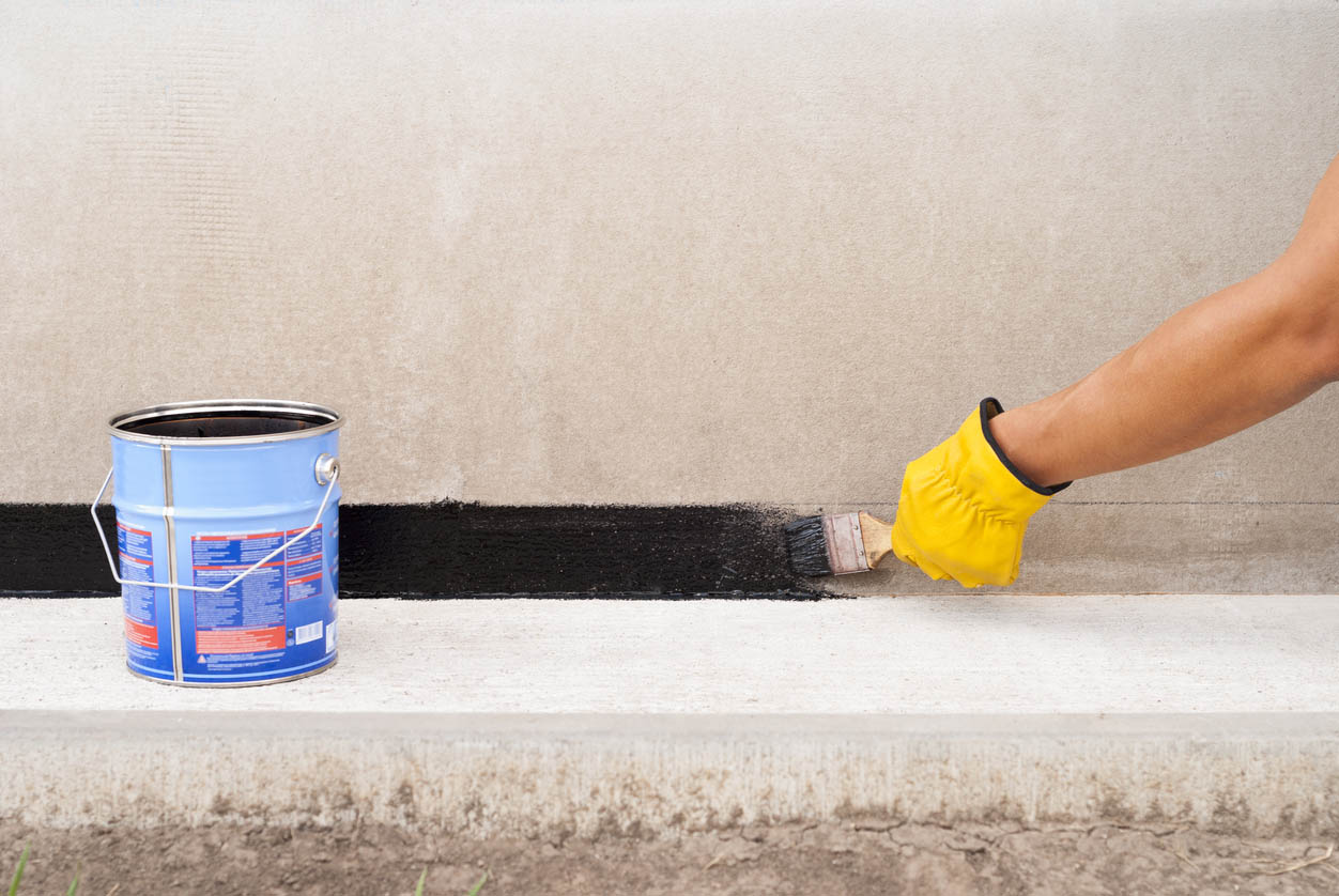 A view of a worker painting a home's foundation.