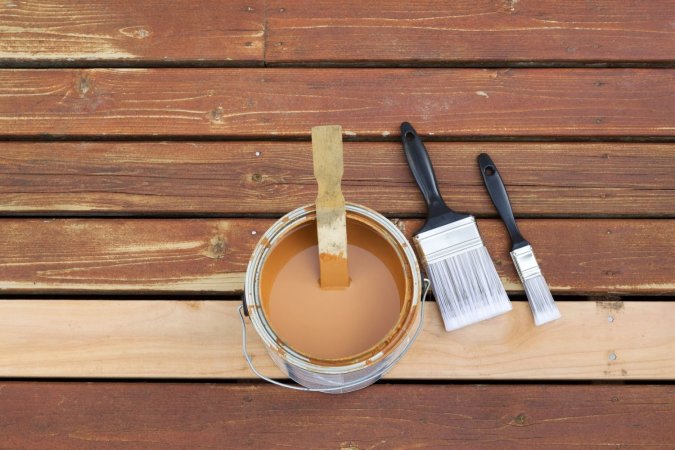 An open can of wood stain sitting on a deck next to 2 paint brushes