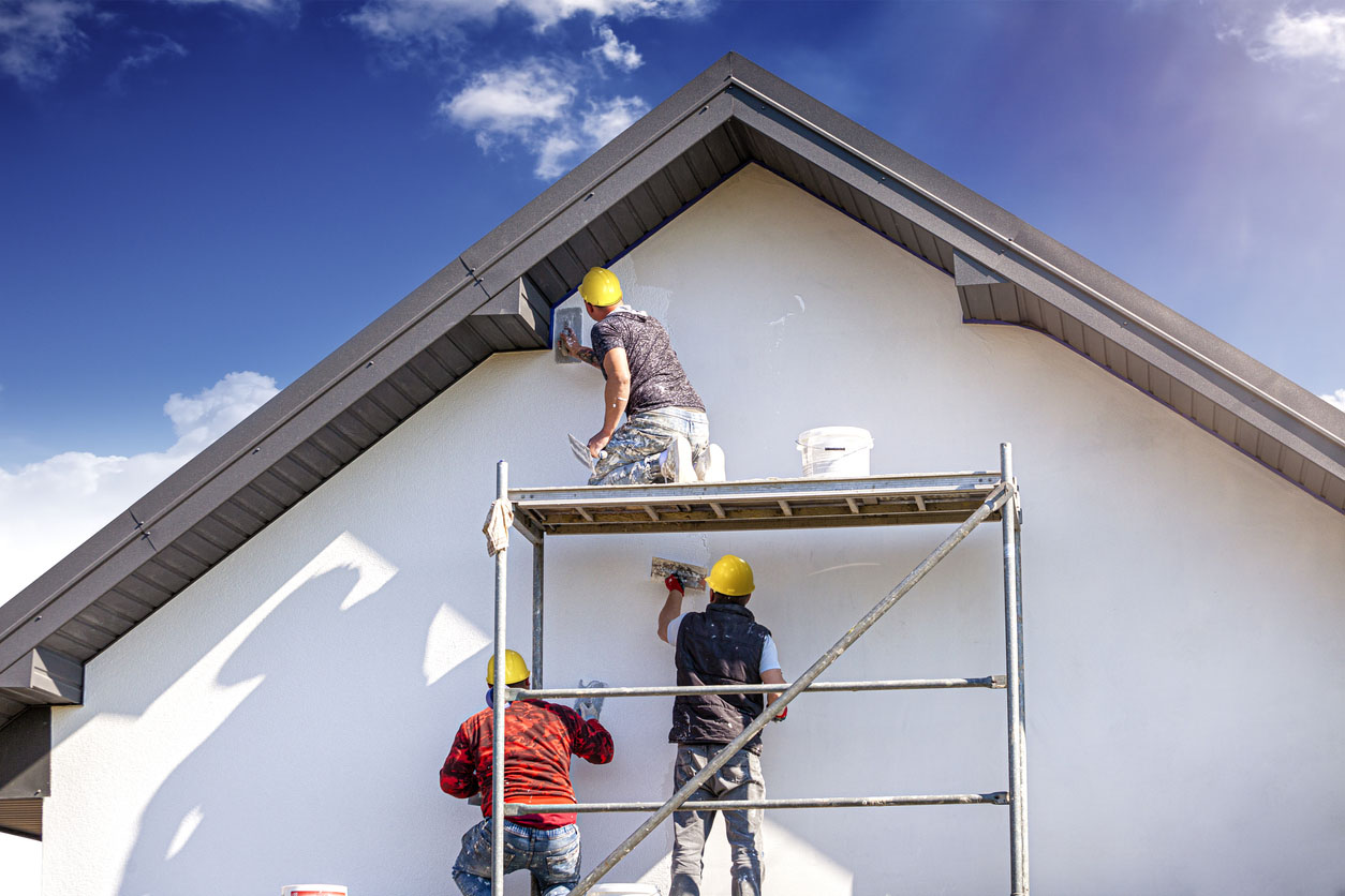 Three workers stand on scaffolding to paint the exterior of a house.