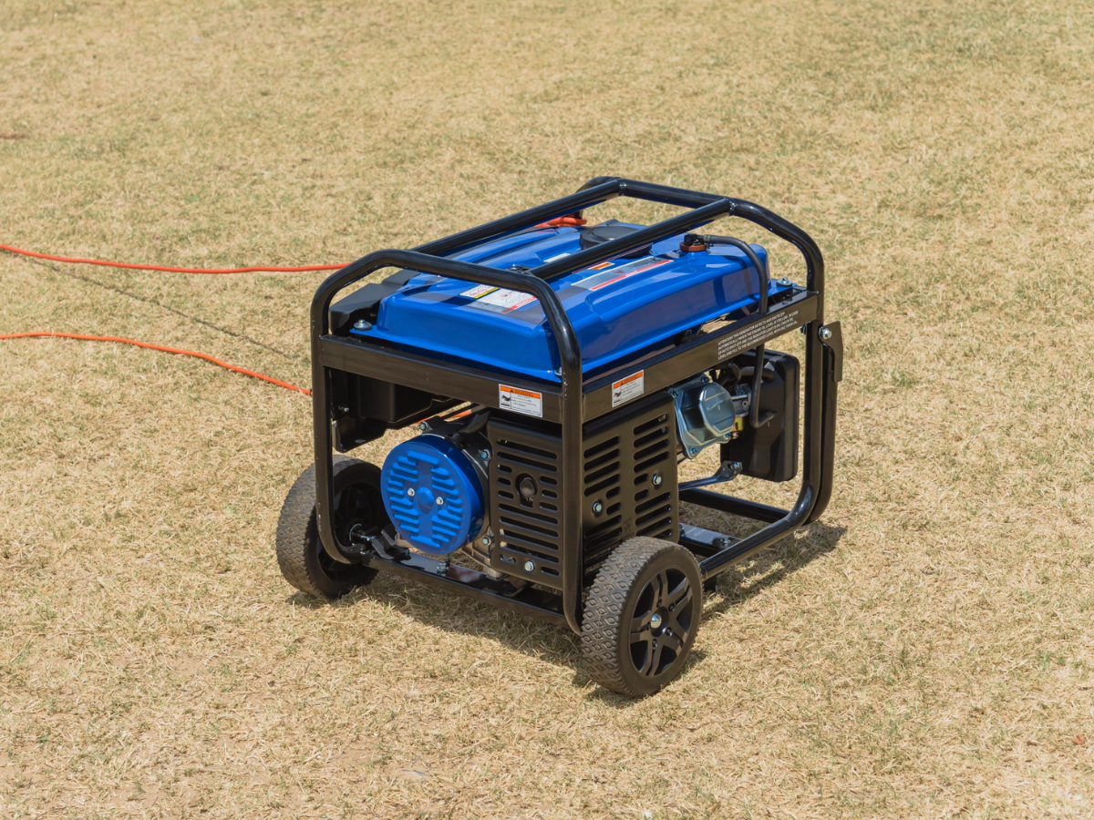 A blue portable electric generator placed in a residential yard is connected to two orange extension cords.