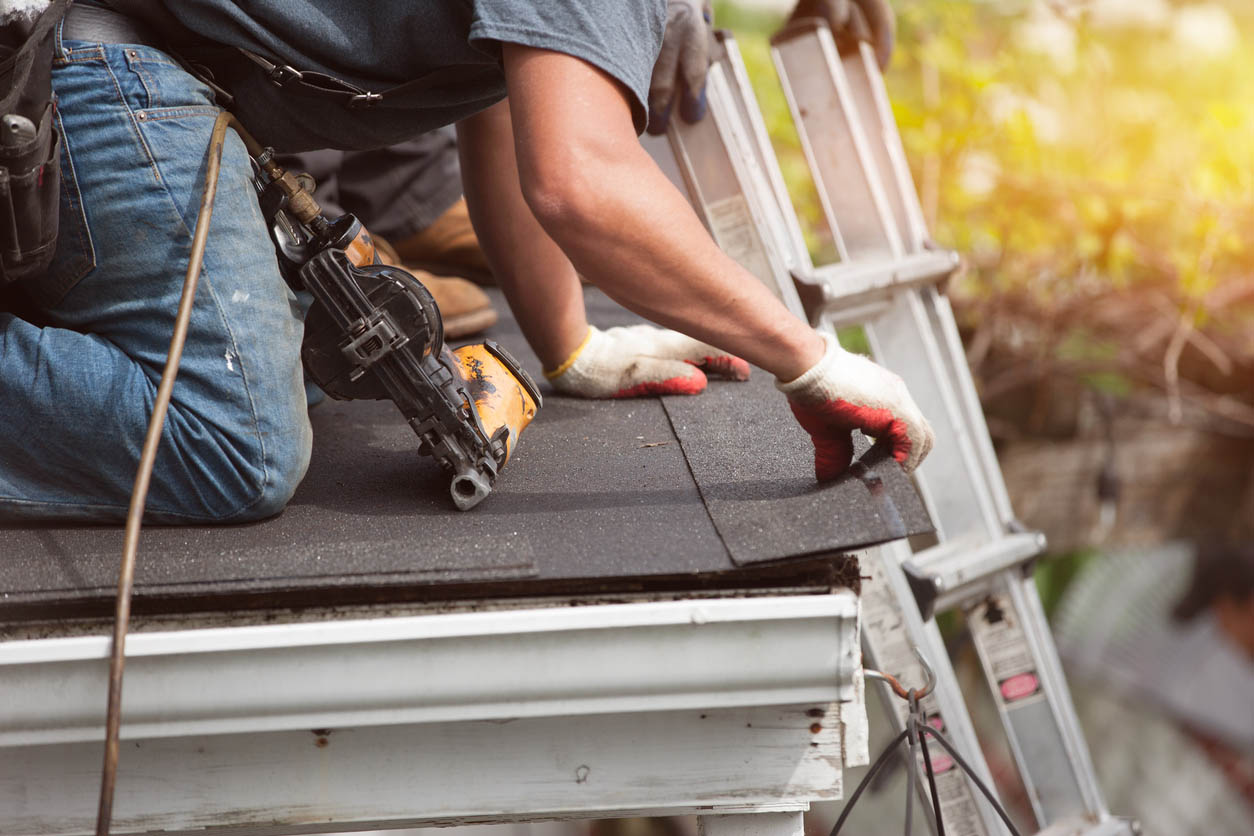 A worker is in the process of installing a new asphalt roof.