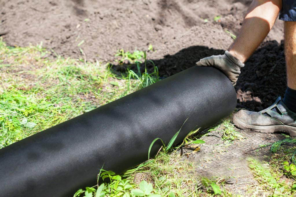 A person laying black landscape fabric onto the ground. 