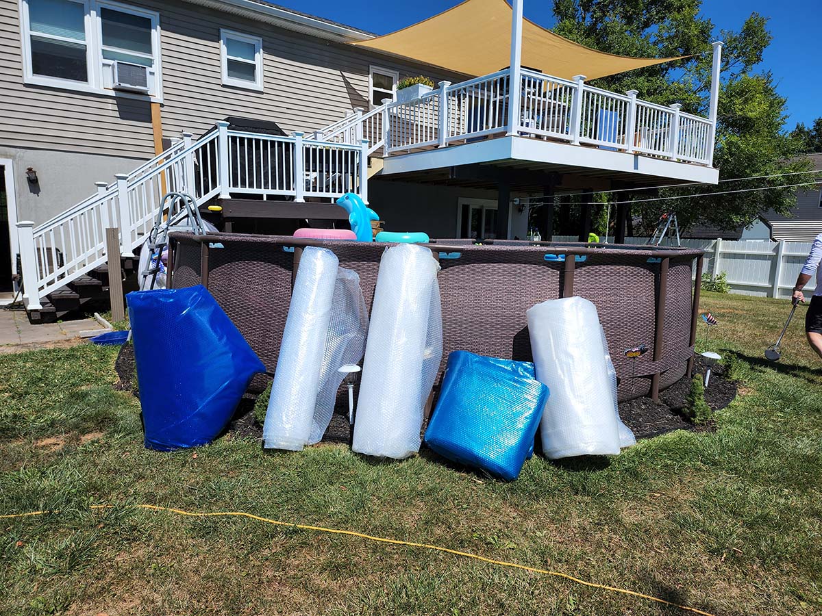 5 rolled up solar pool covers lined up against an above ground pool