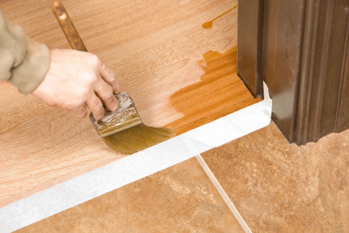 Someone using a paint brush to apply stain to wood flooring