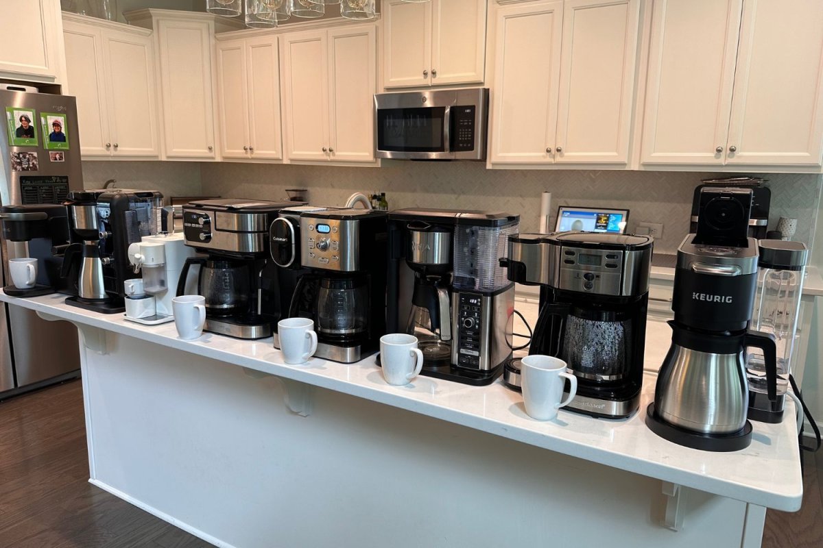 A lineup on a kitchen island of the best dual coffee makers next to waiting coffee mugs