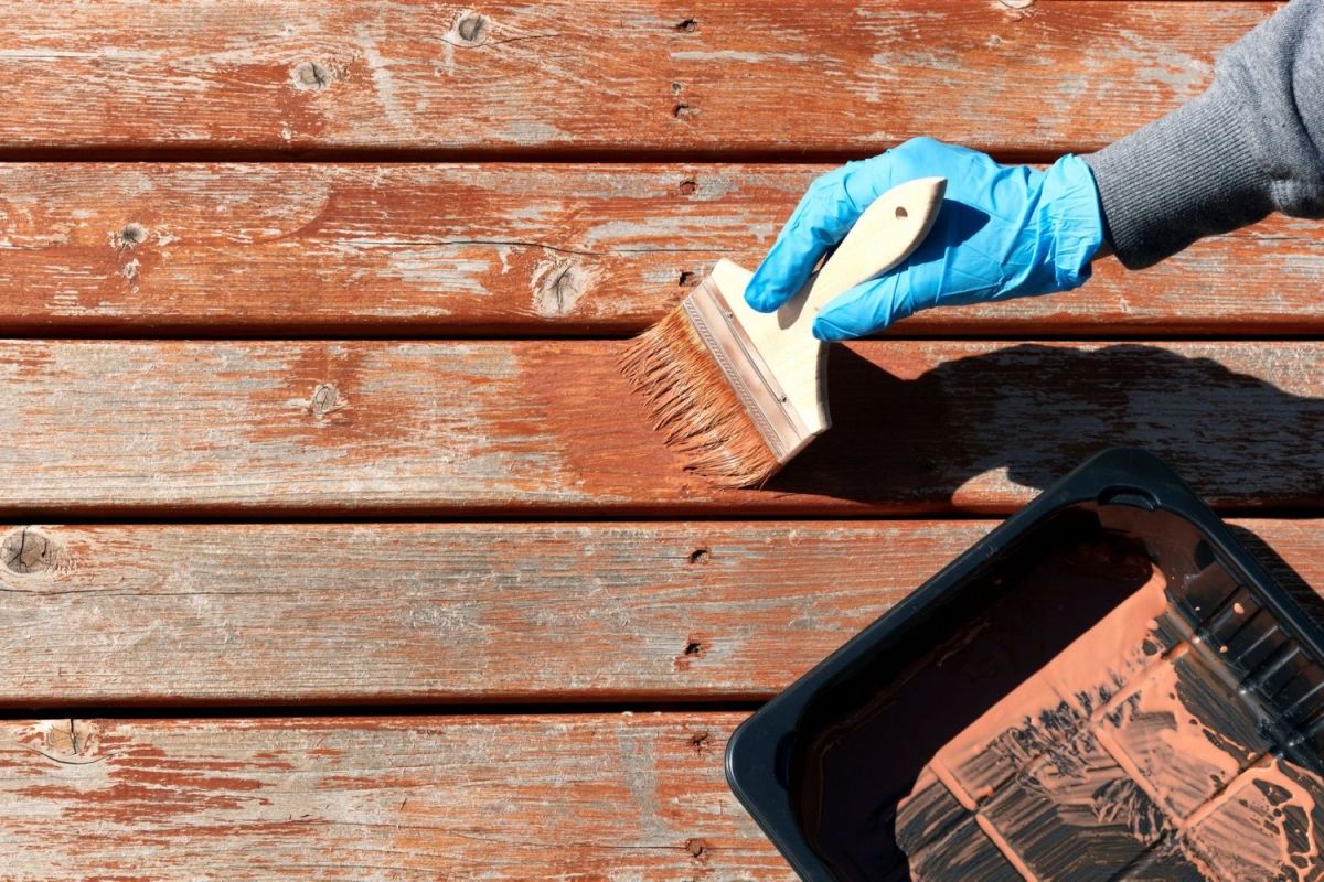 Someone wearing gloves painting a wooden deck