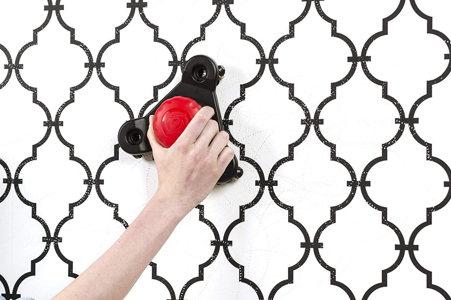 Persons using a black and red scoring tool to remove wallpaper with a white and black trellis design