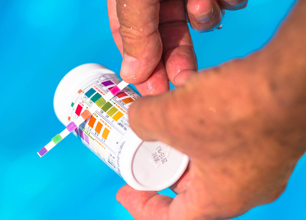 A person is comparing a pool test kit strip to the bottle while testing the water in a pool.