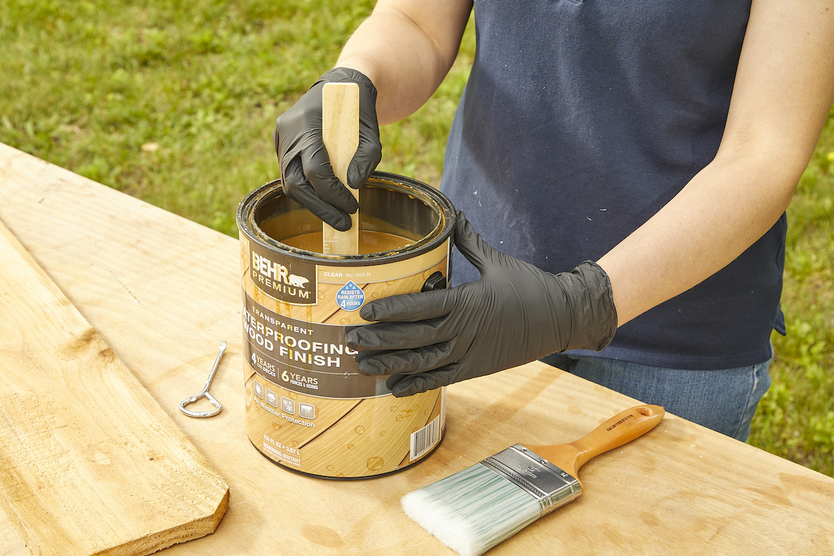 Woman stirs a gallon of wood stain using a wood stirring stick.