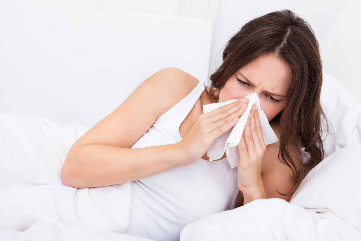 Young Woman Lying On Bed Infected With Allergy Blowing Her Nose