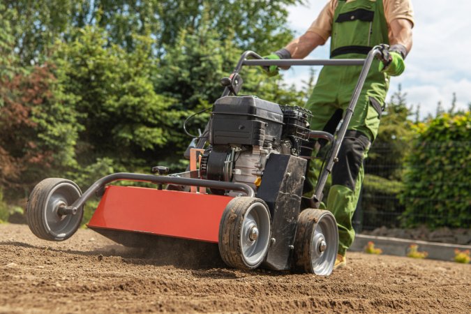 Gardener pushes a lawn aerator and prepares soil for a grass turf installation.