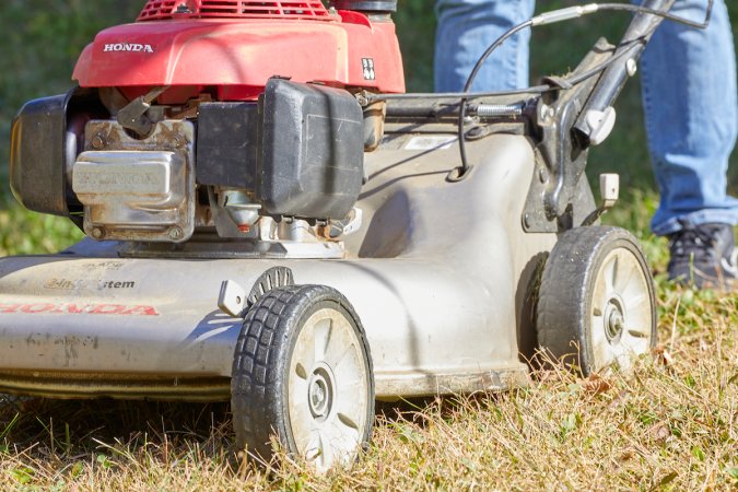 Close up view of the bottom half of a lawn mower, dusty in the grass.