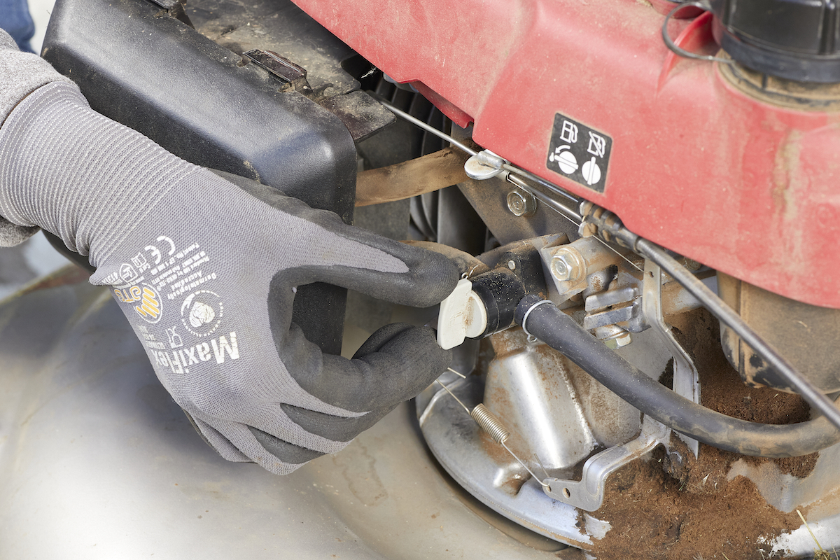 Person wearing gloves switches the gas supply line on a lawn mower on and off.