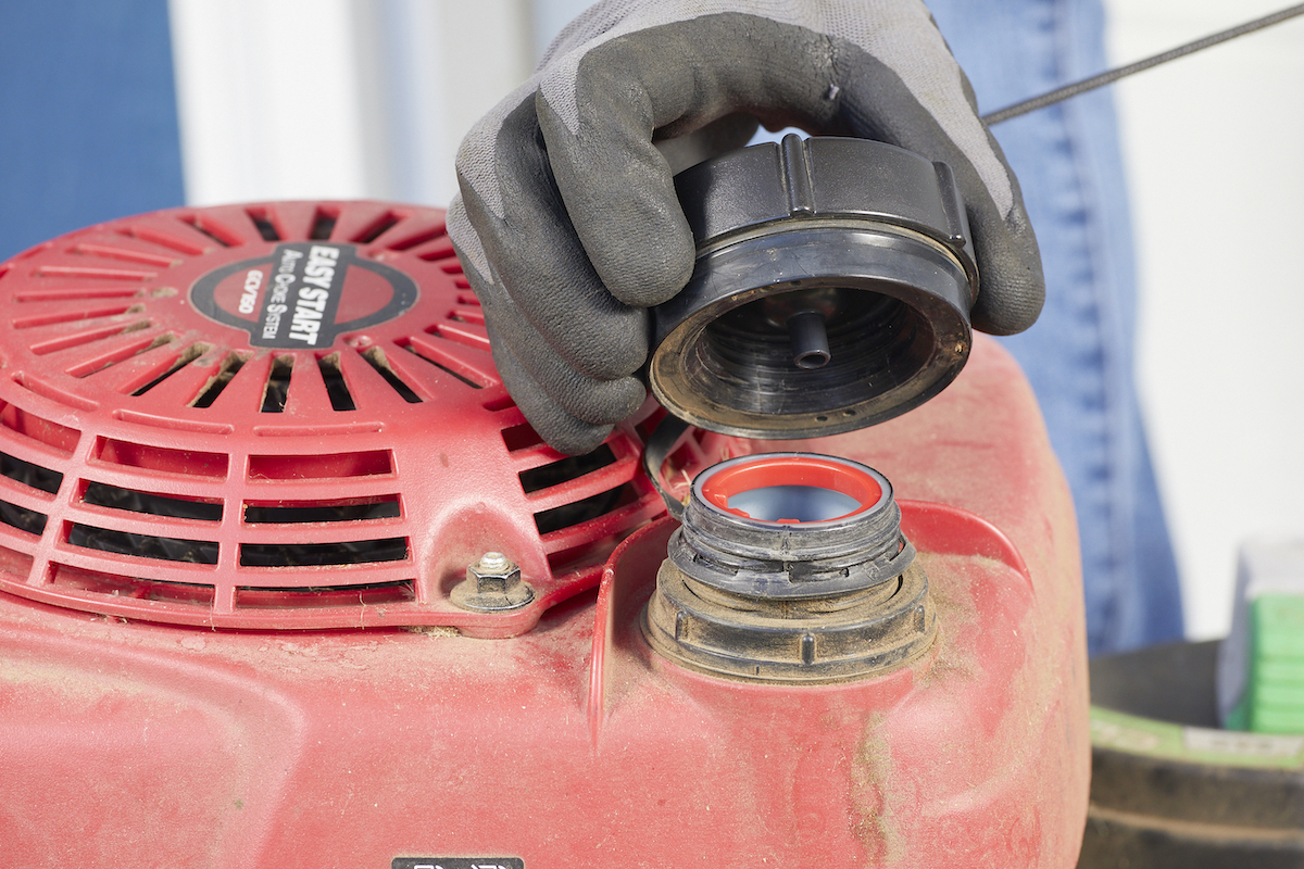 Person wearing black work gloves removes gas cap from a lawn mower.