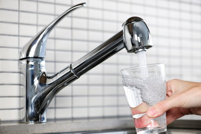 A person getting a glass of water from a kitchen faucet that's hooked up to the best whole house water filter option