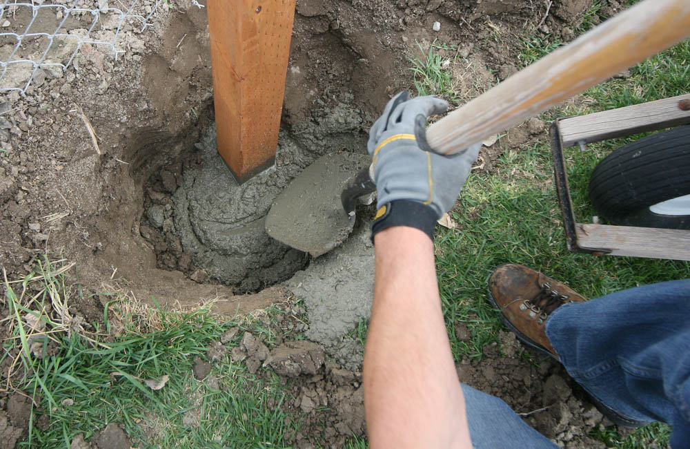 Adding wet concrete to a dug hole around a fence post.