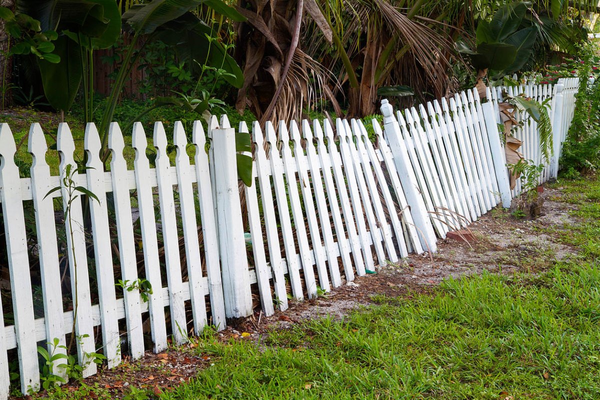 A white picket fence with portions leaning backward.