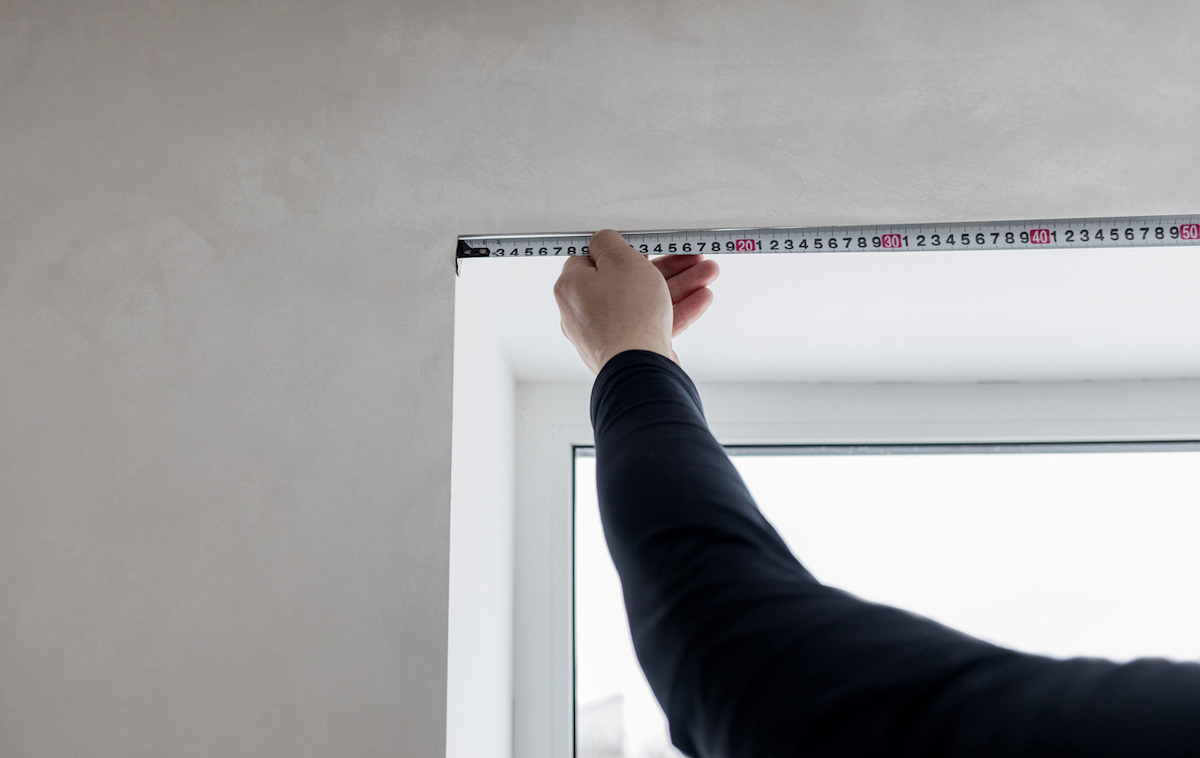 A person is measuring a window with a tape measure.