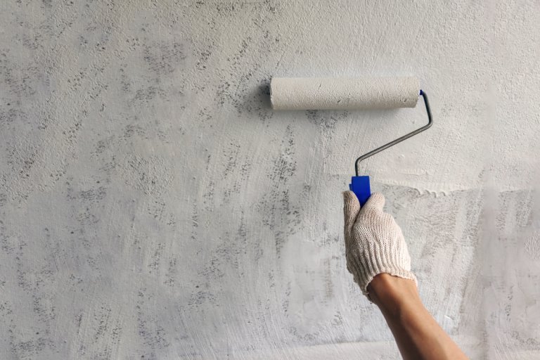 A girl paints a wall with white paint hand with roller for painting close up.