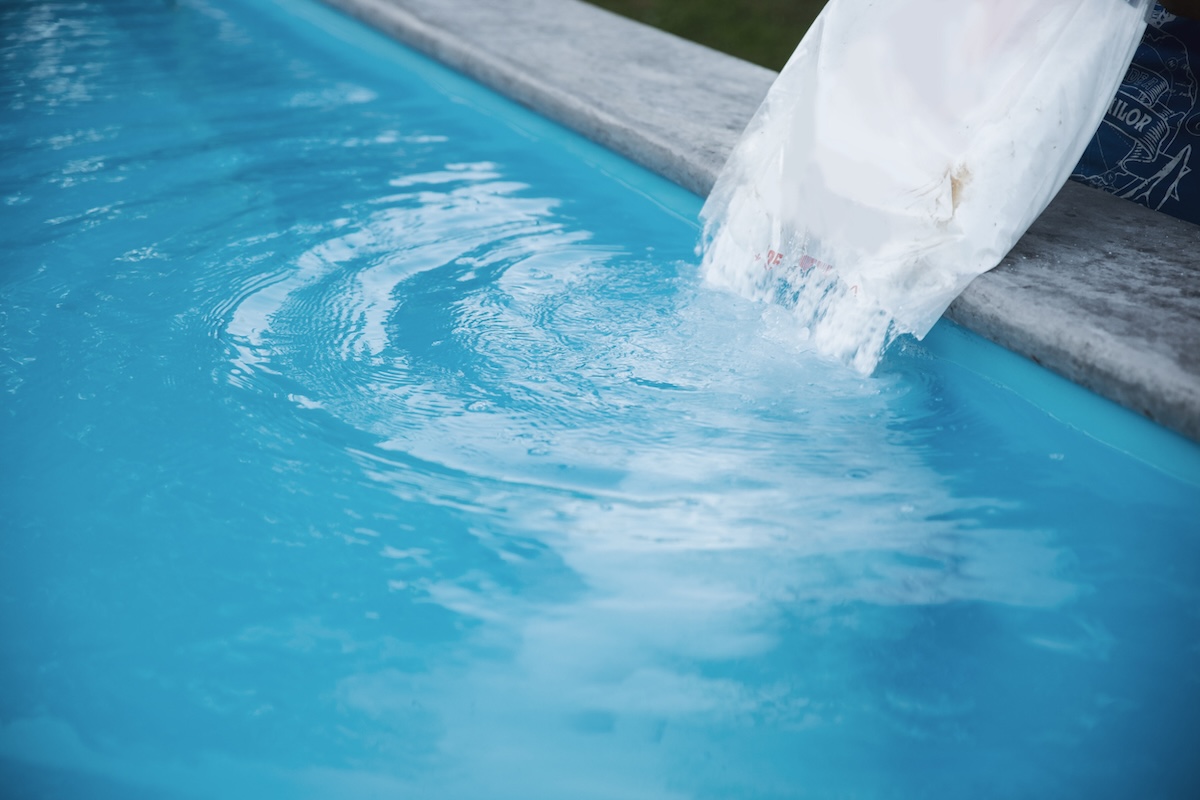 Pouring a bag of salt into a blue, saltwater pool.