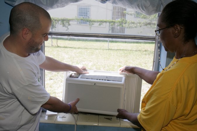 Man and woman place a window air conditioning unit in a window from the inside of a home.