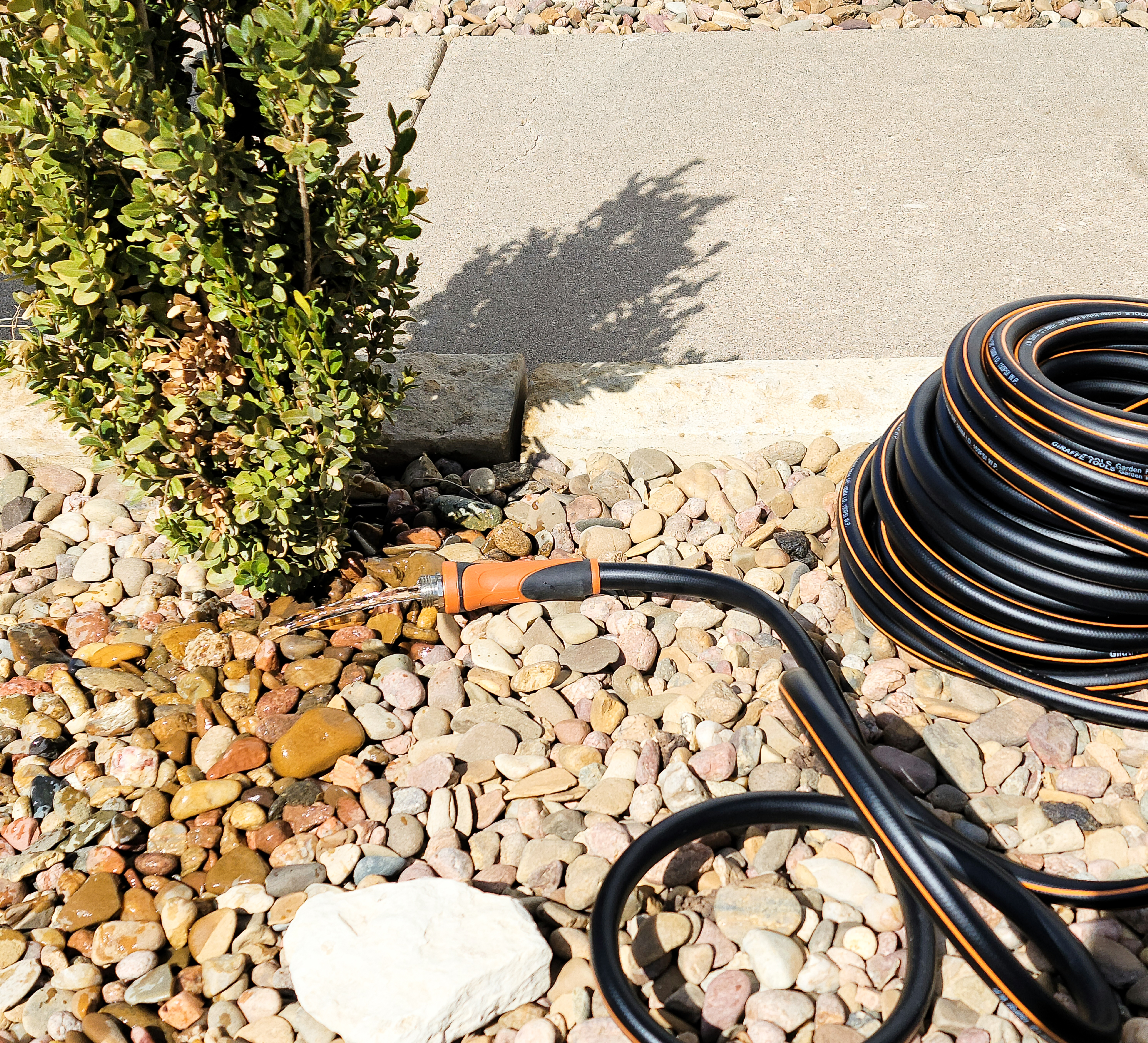 Black garden hose laid on rocks with water flowing