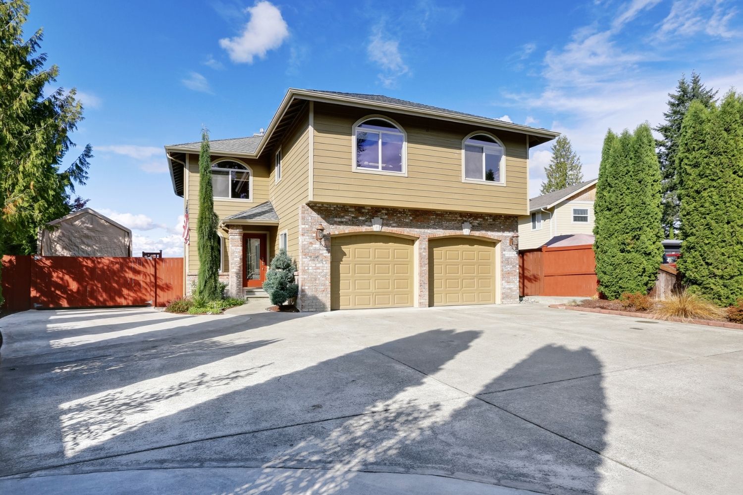 A large concrete driveway leads to a beige house.