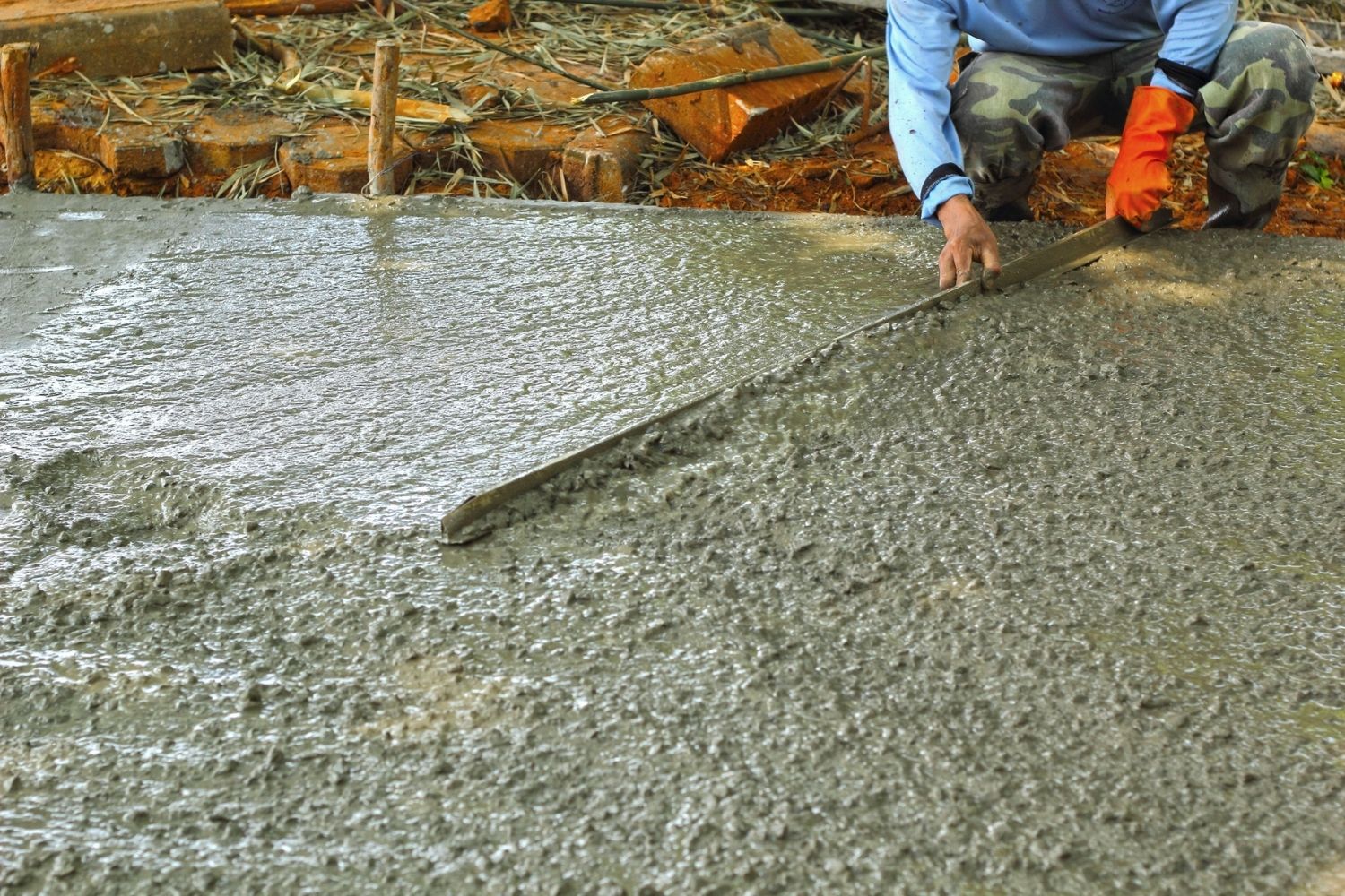 A worker pours and levels concrete in a driveway.