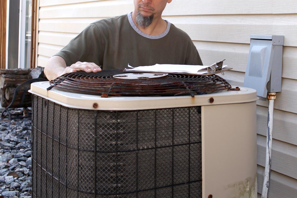 A worker inspects the circuit on an older model air conditioning unit.