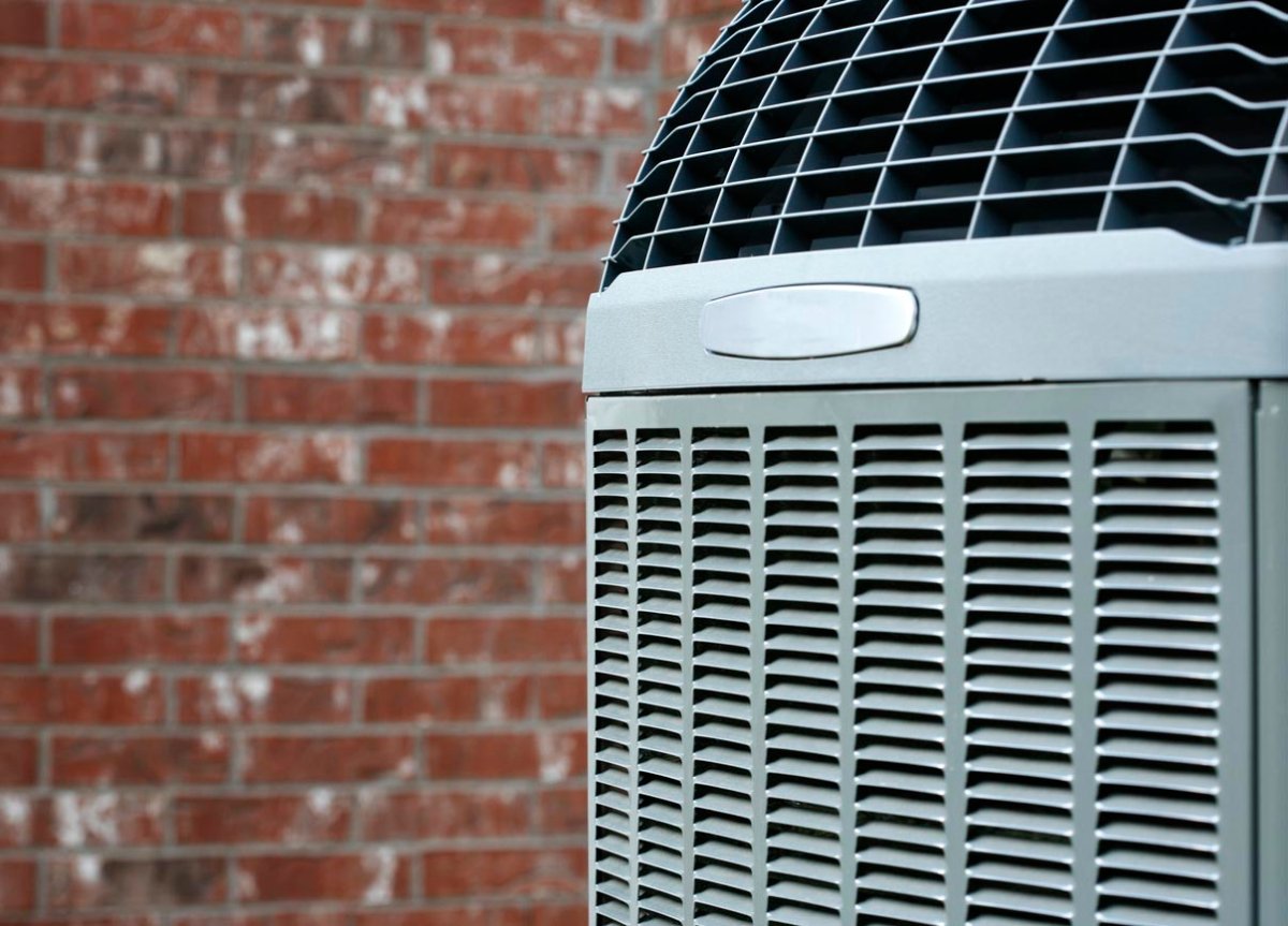 An outside air conditioning unit with a brick wall in the background.