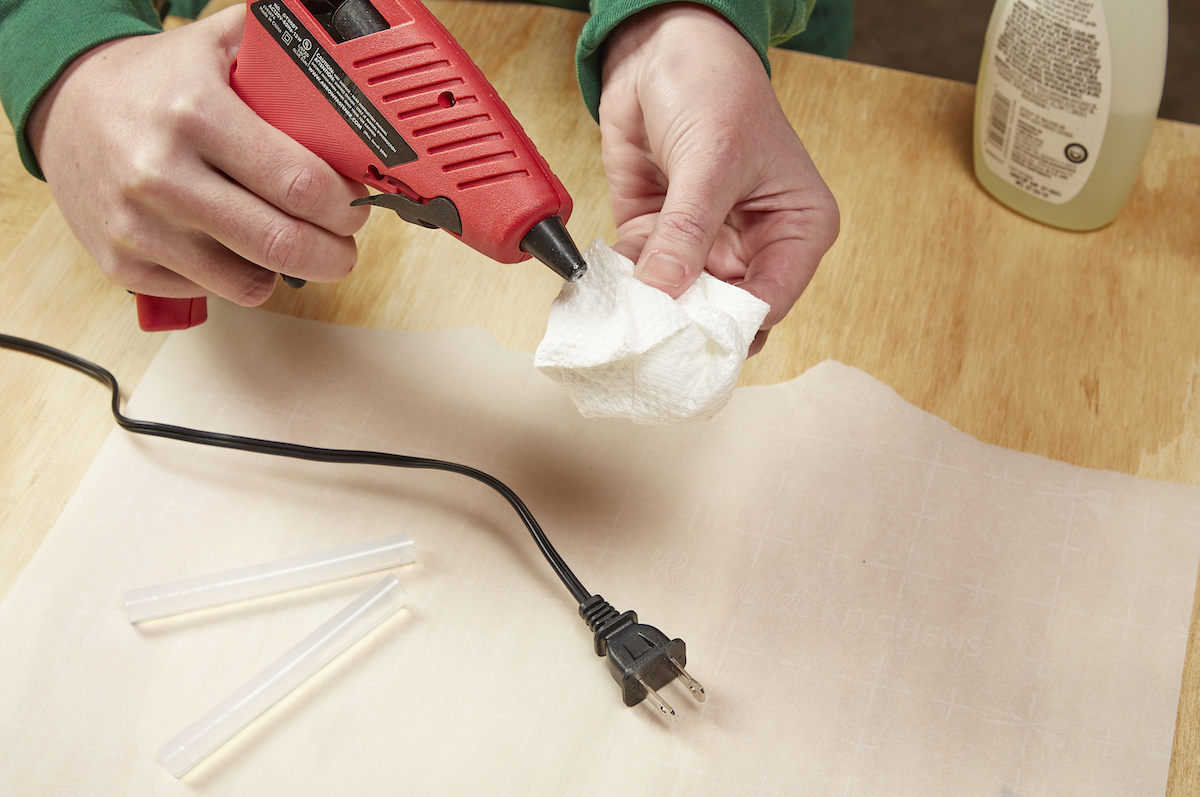 Woman uses acetone on a cotton square to clean the nozzle of a hot glue gun.