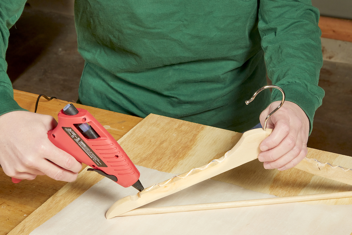 Woman applies hot glue via glue gun onto a wooden hanger.